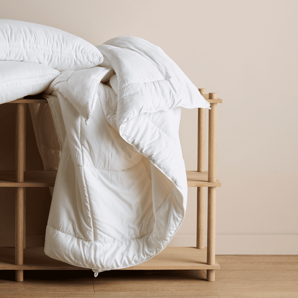 A bamboo comforter and pillows hanging off a wooden piece of furniture.