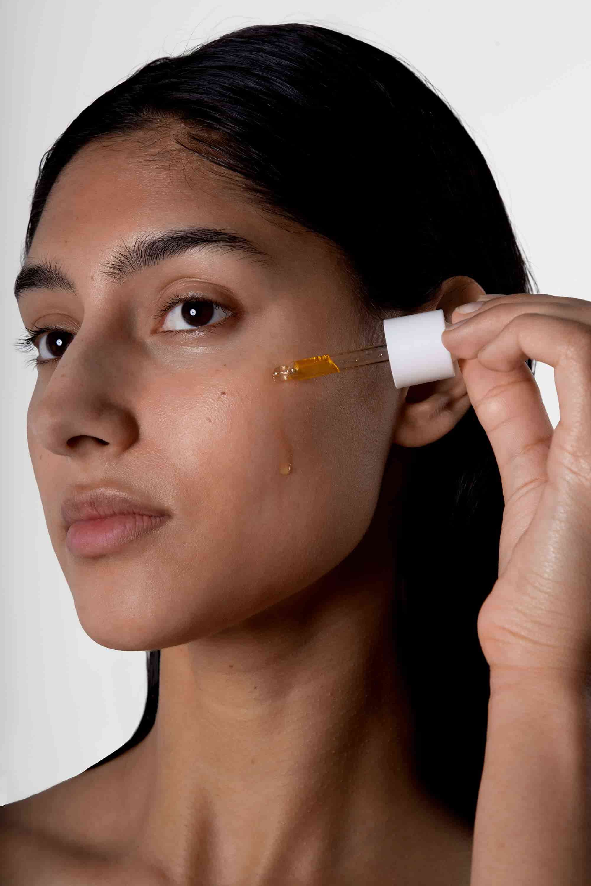 A woman applies a drop of the Vitamin C elixir onto her cheek.